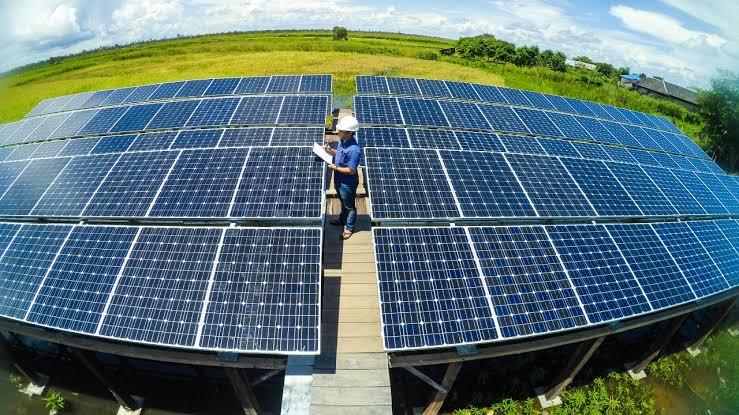 Seorang teknisi memeriksa panel surya di atap sambil mencatat