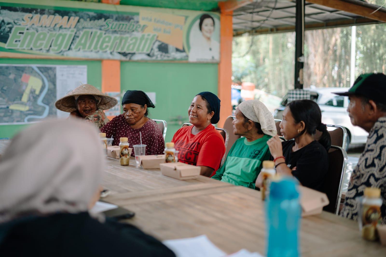 Community members at a village meeting under a banner about waste as an alternative energy source