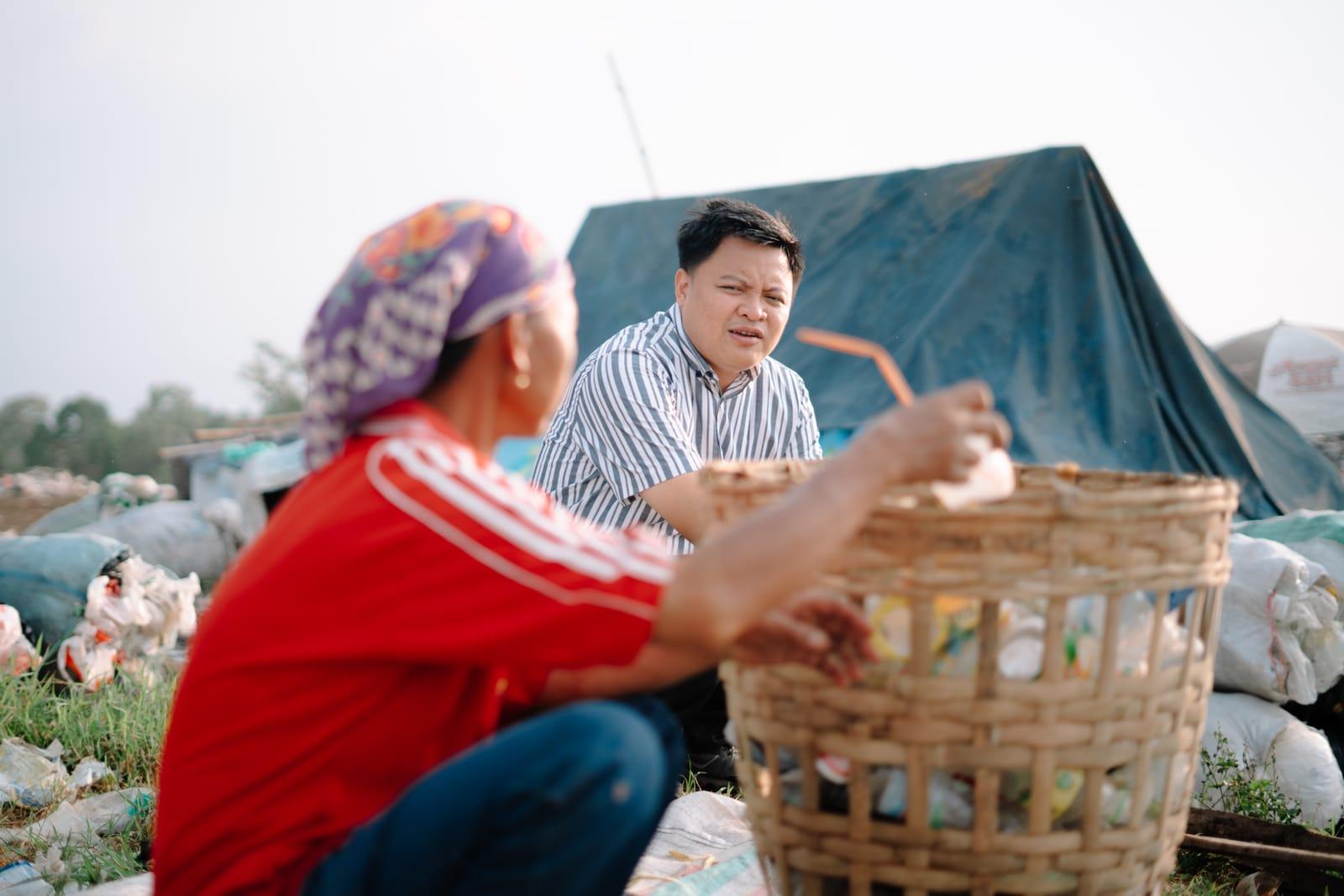 A government official speaks with an informal waste picker holding a basket of sorted plastic packaging waste