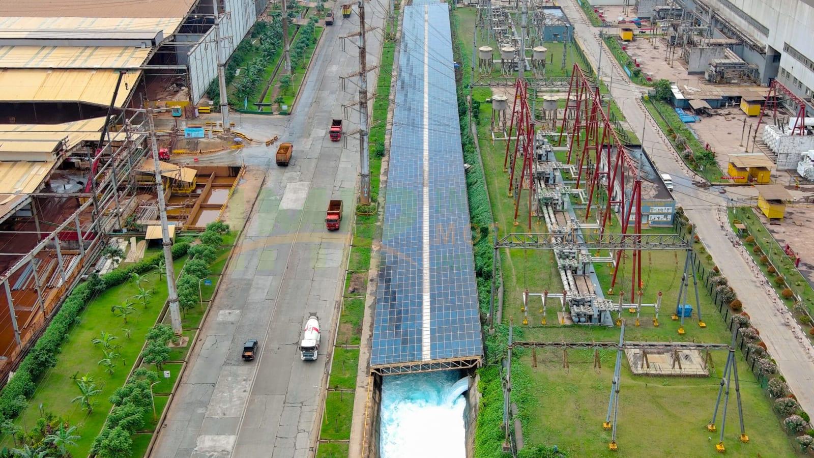 Foto udara panel surya yang menutupi atap pabrik besar dan sebuah kanal di dalam kawasan industri Morowali, dengan bangunan smelter dan perbukitan di latar belakang