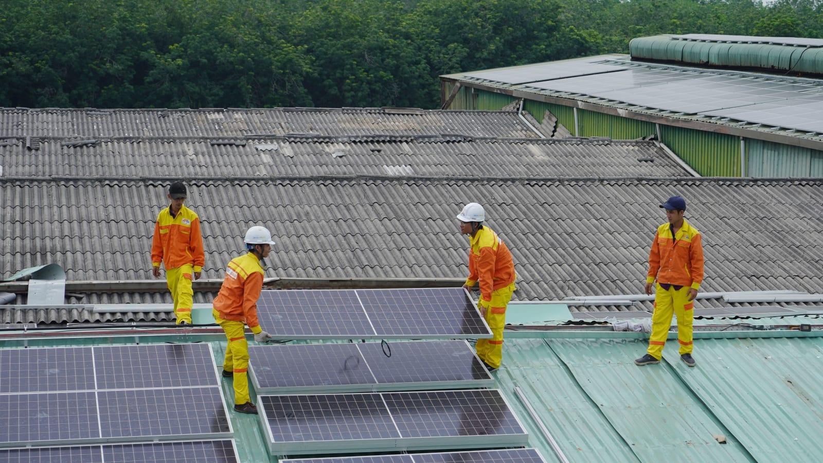 Engineers and officials reviewing solar project plans on a table with laptops in a bright Jakarta meeting room, with a rooftop solar array visible through the window
