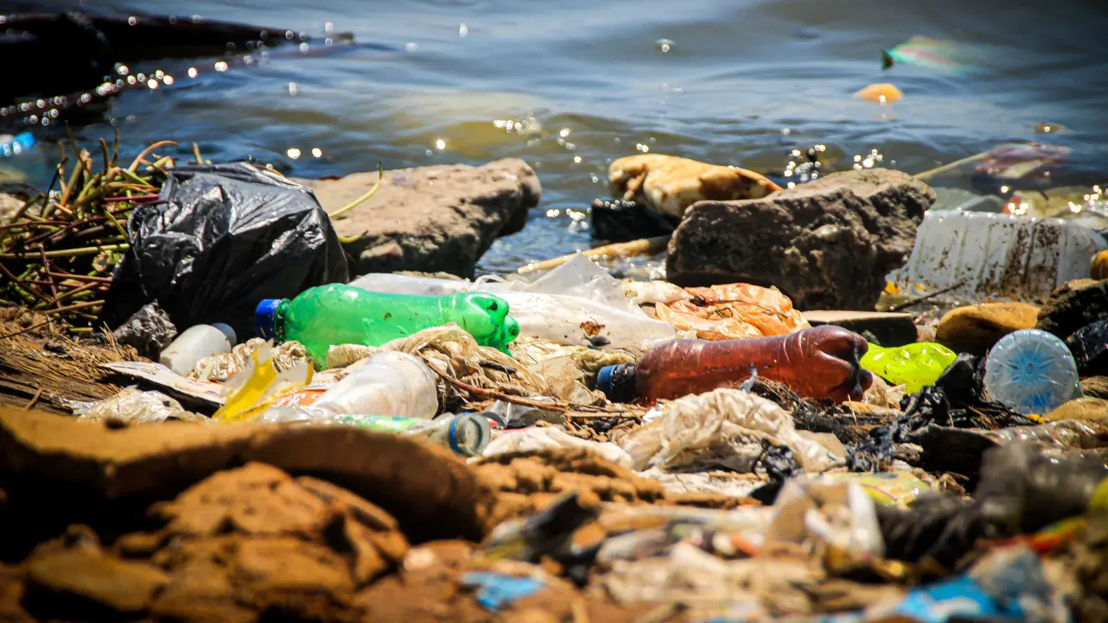 A river mouth trash boom catching floating plastic waste before it reaches the coast, with a collection crew working from a small boat