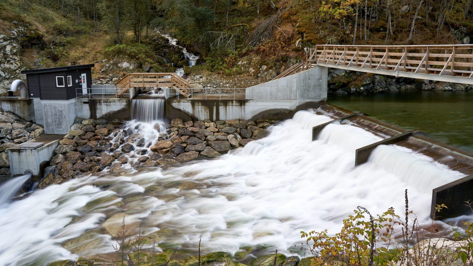 Hydropower dam, penstocks and turbine house in a forested river valley in Sumatra, with transmission lines running along the ridge