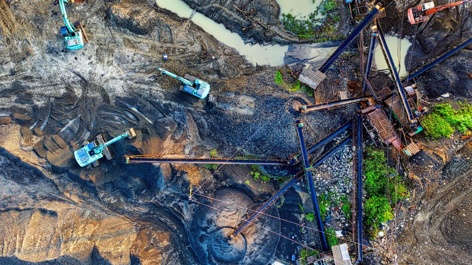 Coal stockpiles and heavy mining equipment at an open-pit site in Kalimantan