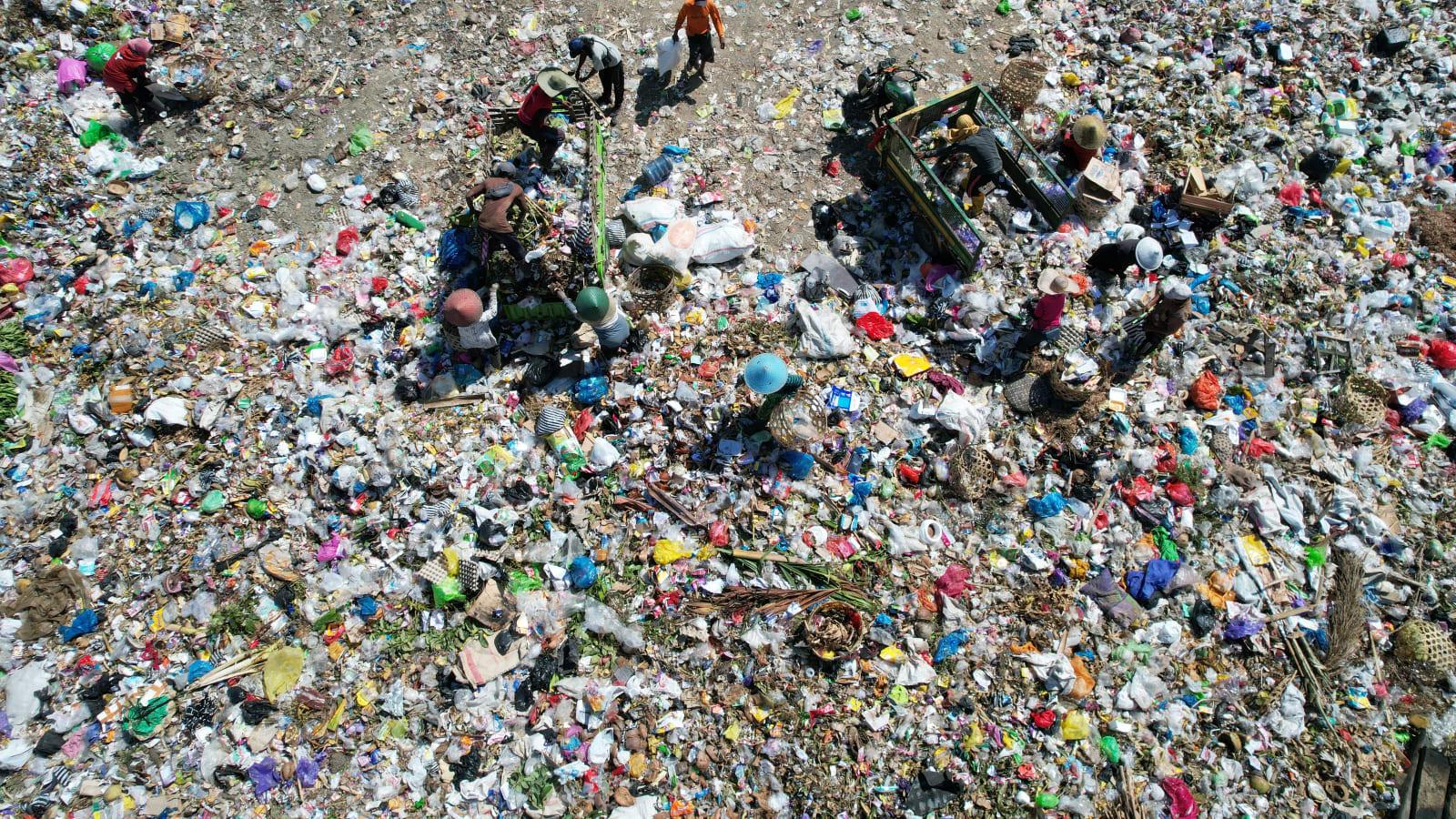 Waste sorting workers in high visibility vests and gloves working a sorting line at an Indonesian recovered fuel plant, with baled material and conveyor equipment behind them