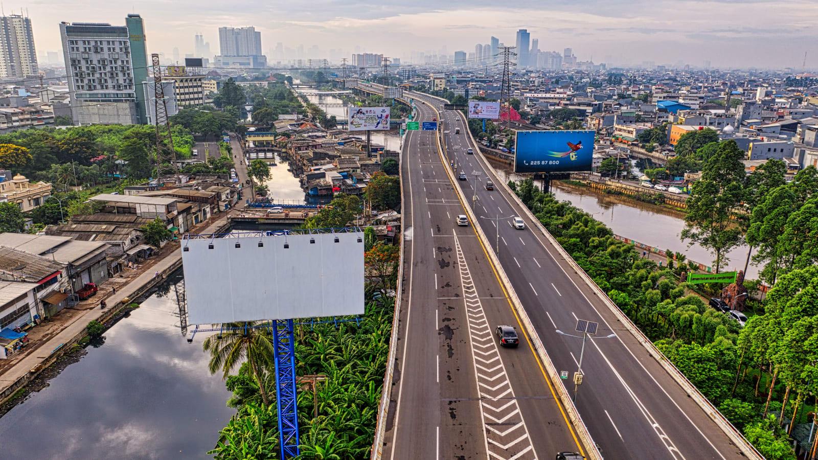Solar panels installed along the edge of an elevated toll road crossing water in Bali, with traffic passing and the sea visible beyond